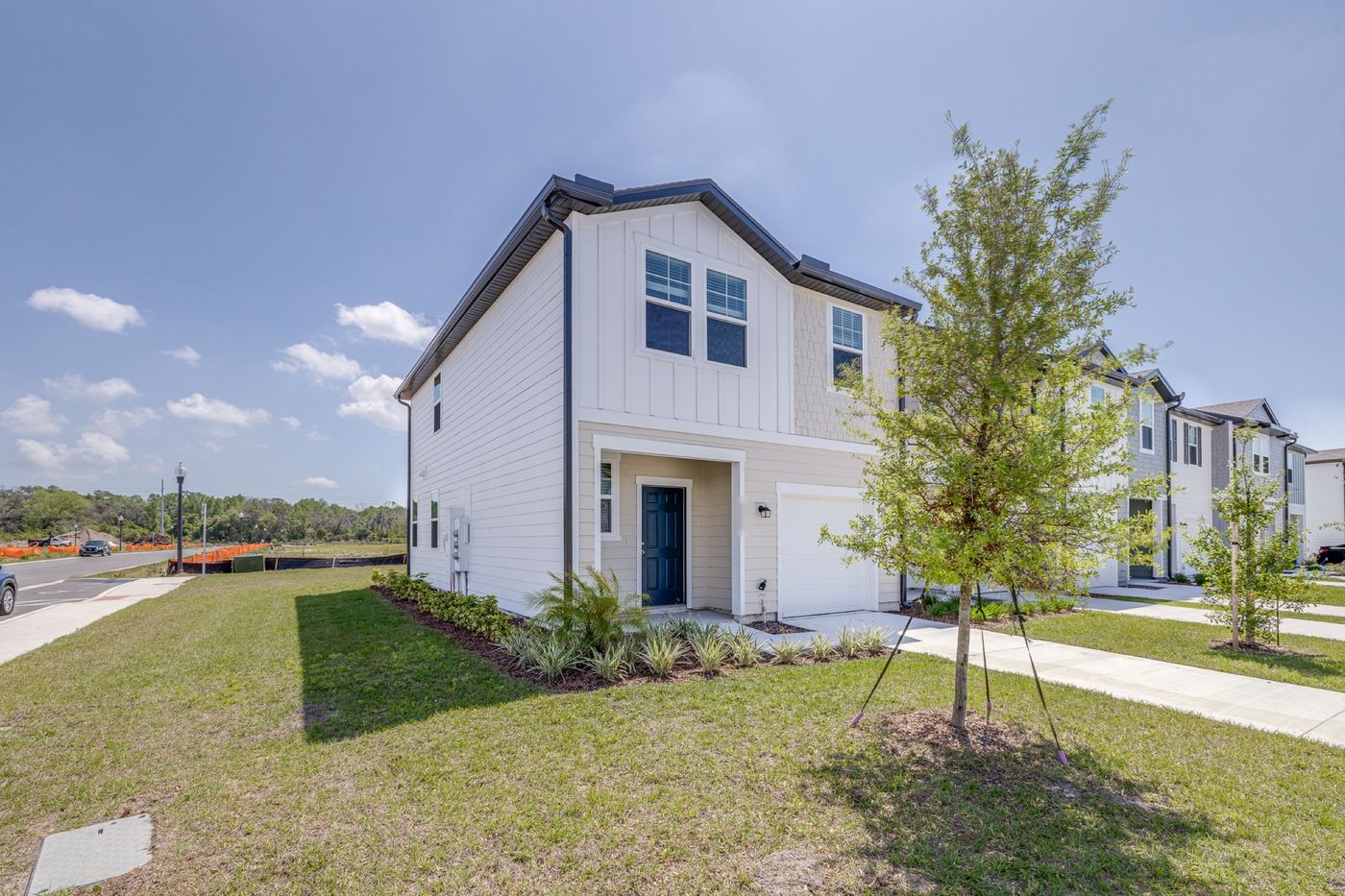 Two-story corner townhome exterior with a young tree and lawn